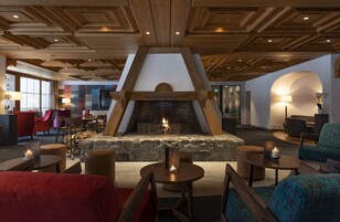 Un lobby acogedor con chimenea de piedra, vigas de madera en el techo, asientos cómodos y una pantalla de televisión grande.