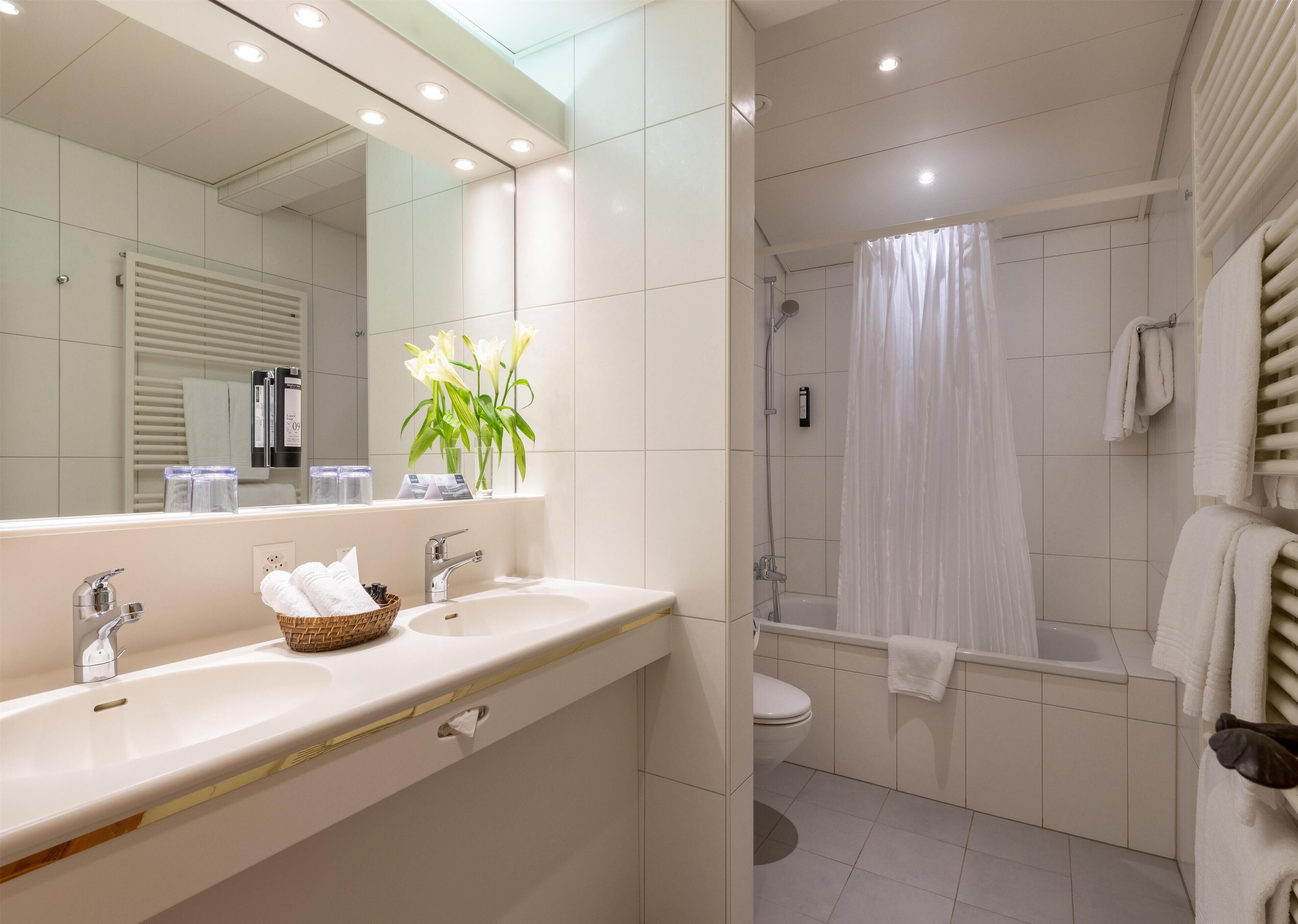 A modern bathroom with a large mirror, a sink with a basket of towels, a shower area, and a toilet.