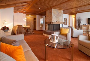 A cozy living room with a fireplace, a glass coffee table, and a dining area with a chandelier. - Sunstar Hotel Grindelwald (Grindelwald)