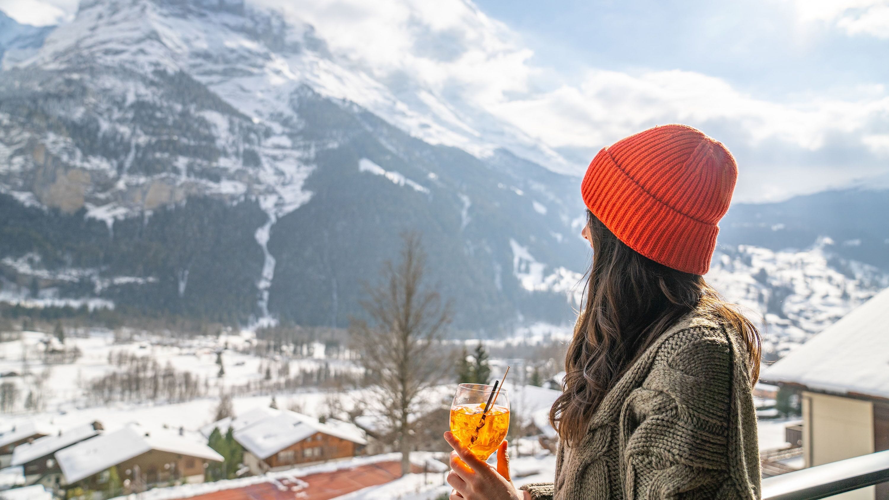 Eine Person hält ein Getränk, im Hintergrund eine Berglandschaft.