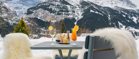 Une table dressée à l’extérieur, avec vue sur la montagne, un verre de jus d’orange et une bouteille d’eau.