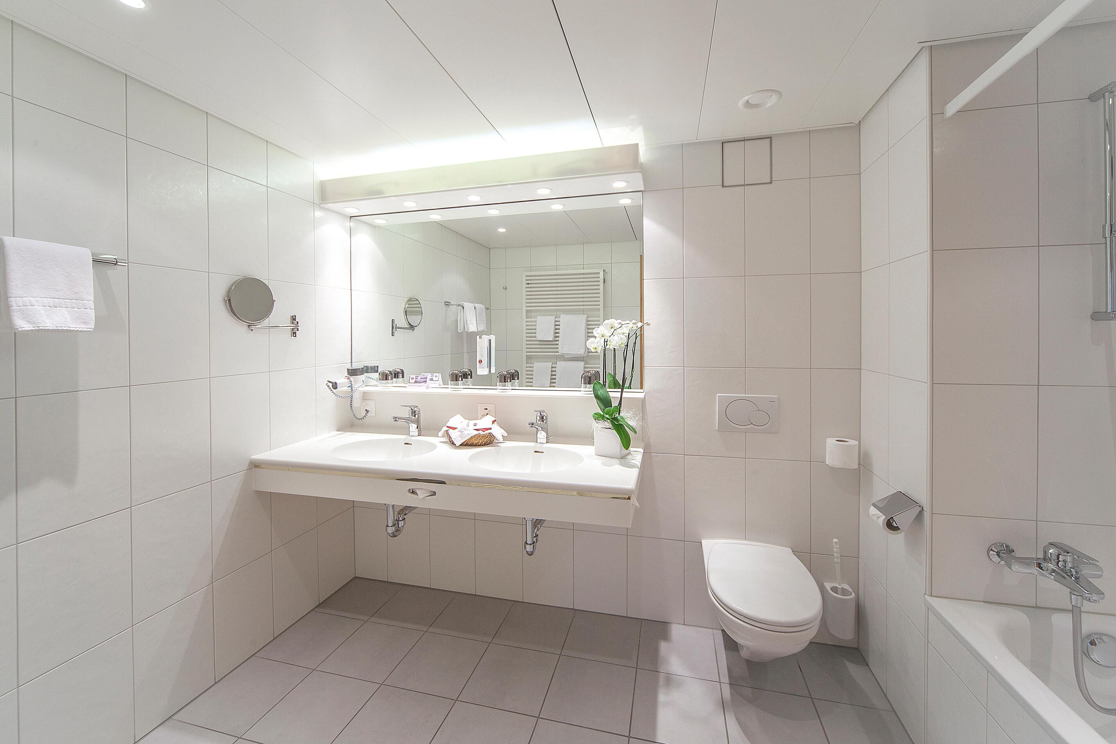 A modern bathroom with a double sink, a toilet, and a bathtub.