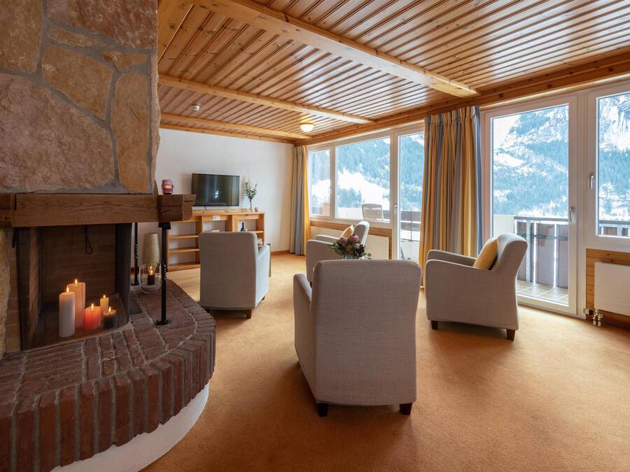 A cozy living room with a stone fireplace, comfortable seating, a television, and large windows offering mountain views.