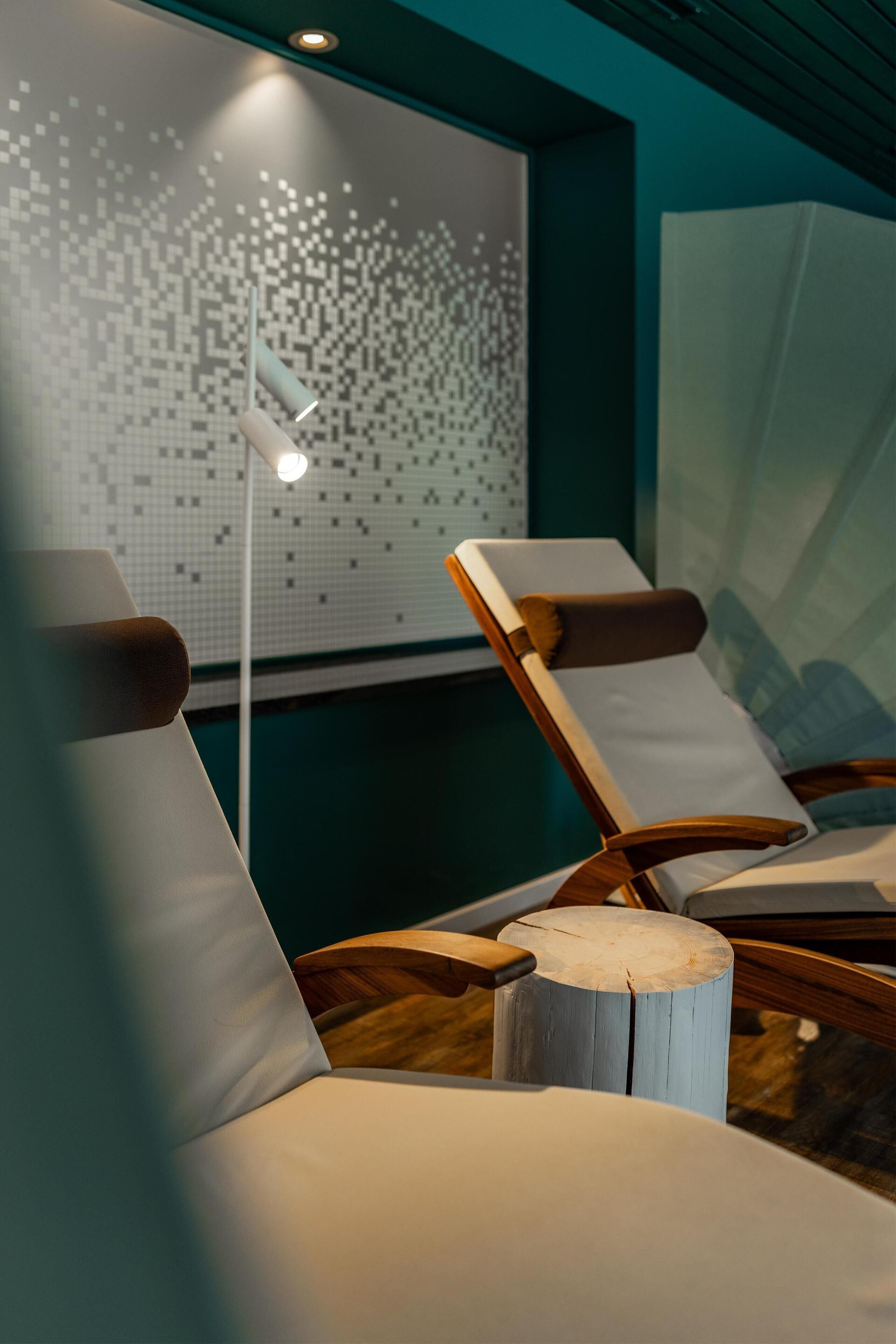 Un cuarto de spa con dos sillones reclinables, una pared con un patrón pixelado y un taburete de madera.