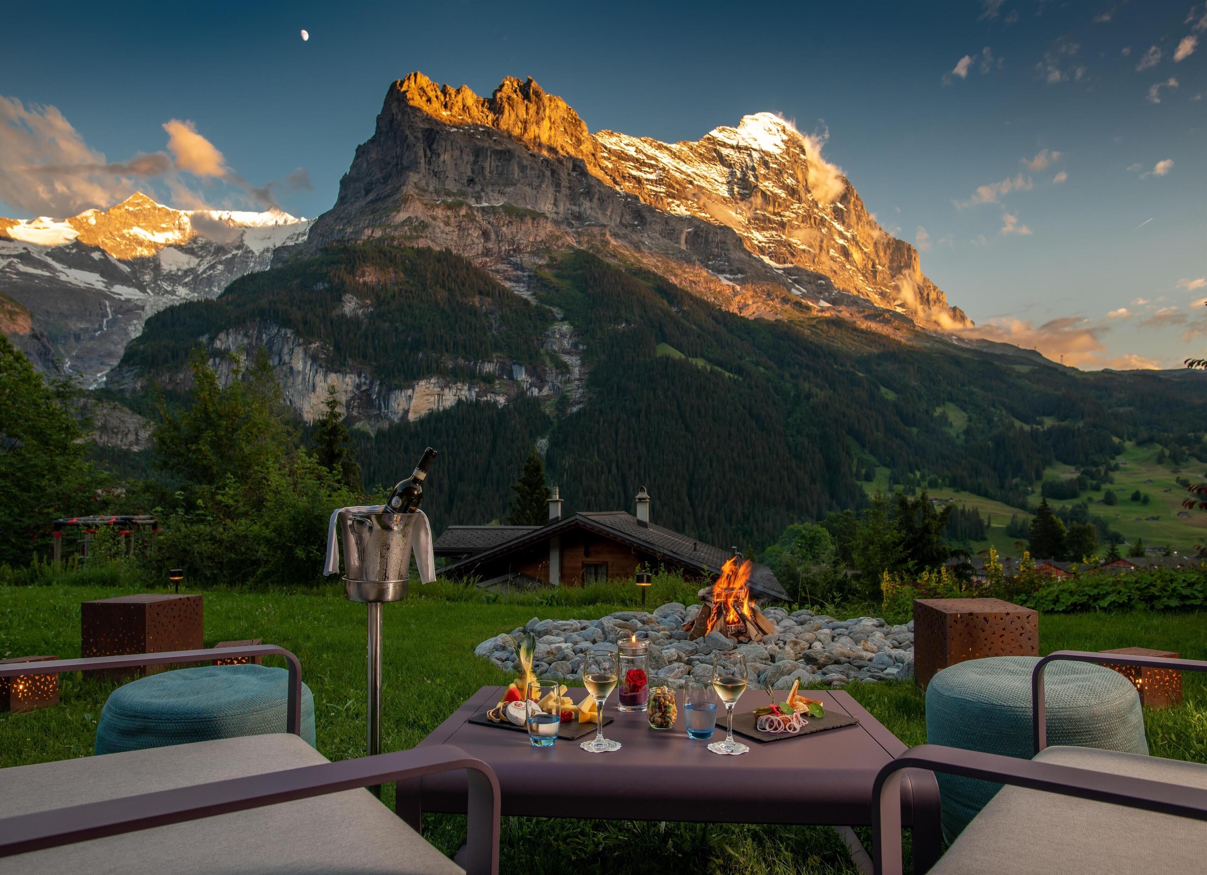 Mesa al aire libre con vista a la montaña, chimenea y una botella de vino.