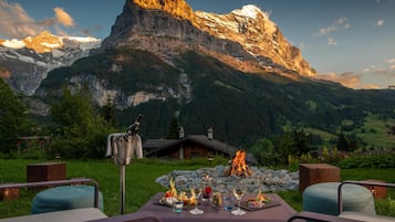 A table set outdoors with a mountain view, a fireplace, and a bottle of wine.