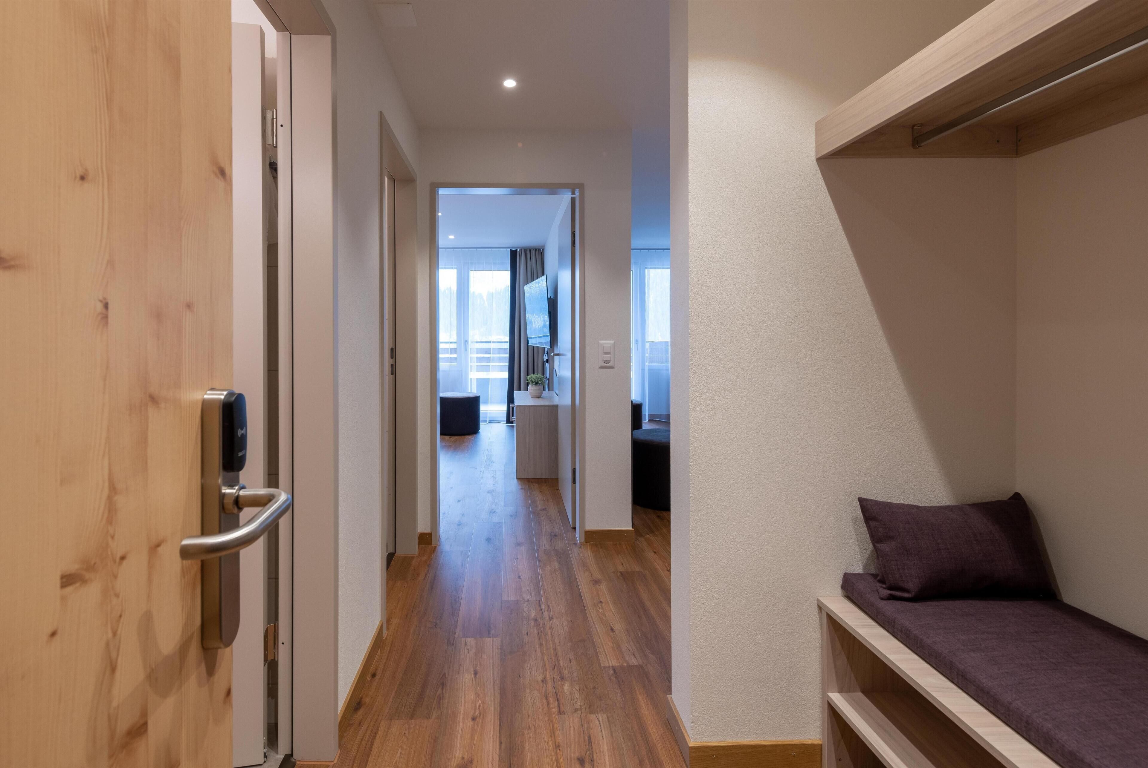 A hallway with wooden flooring, a bed with a headboard, and a door with a handle.