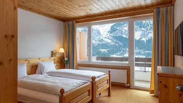 Un dormitorio de madera con una cama, un ventanal con cortinas y vistas a montañas nevadas.