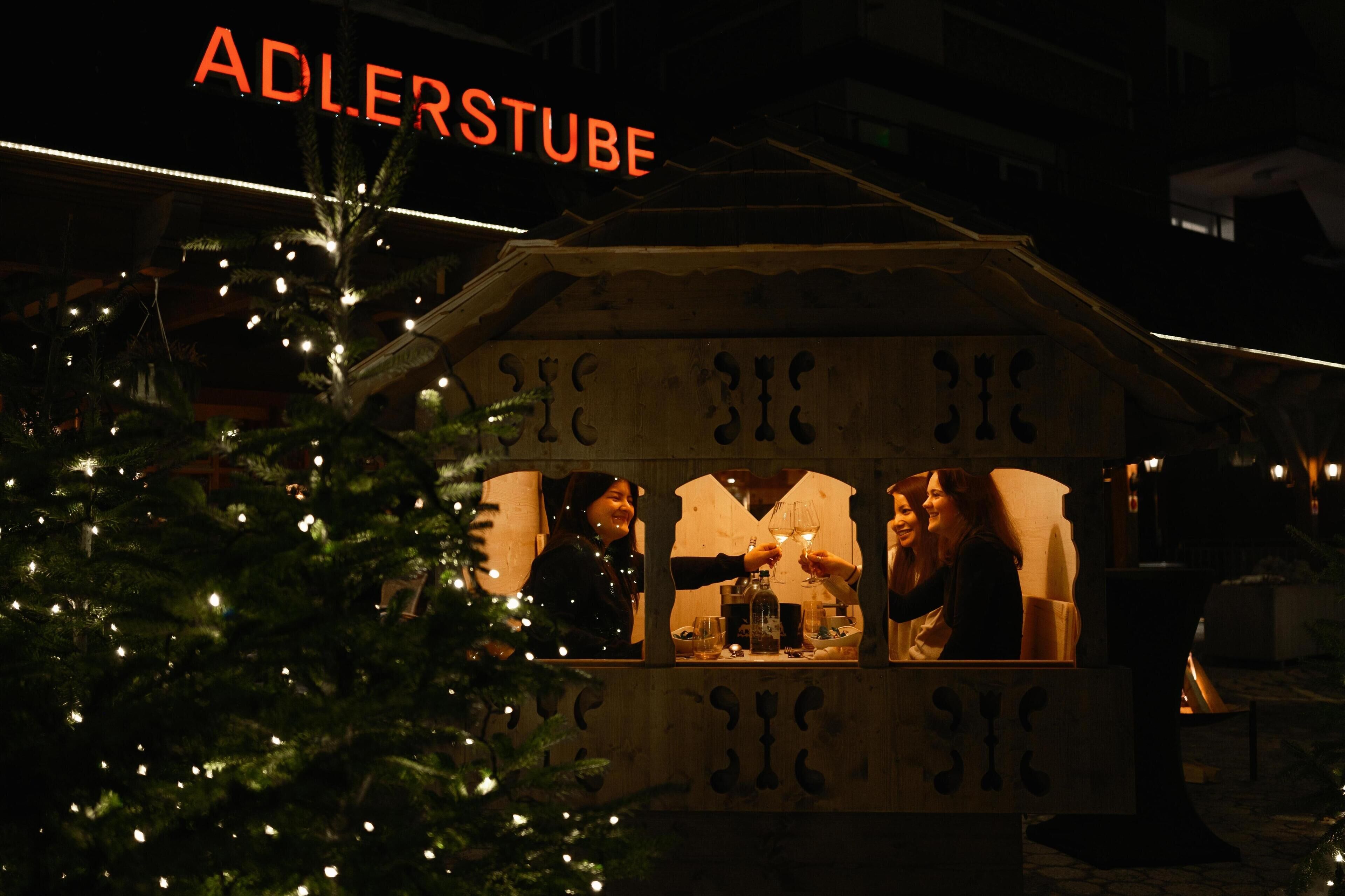A Christmas tree with lights in front of a building with a sign that reads "ADLERSTUBE".