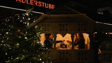 A Christmas tree with lights in front of a building with a sign that reads "ADLERSTUBE".