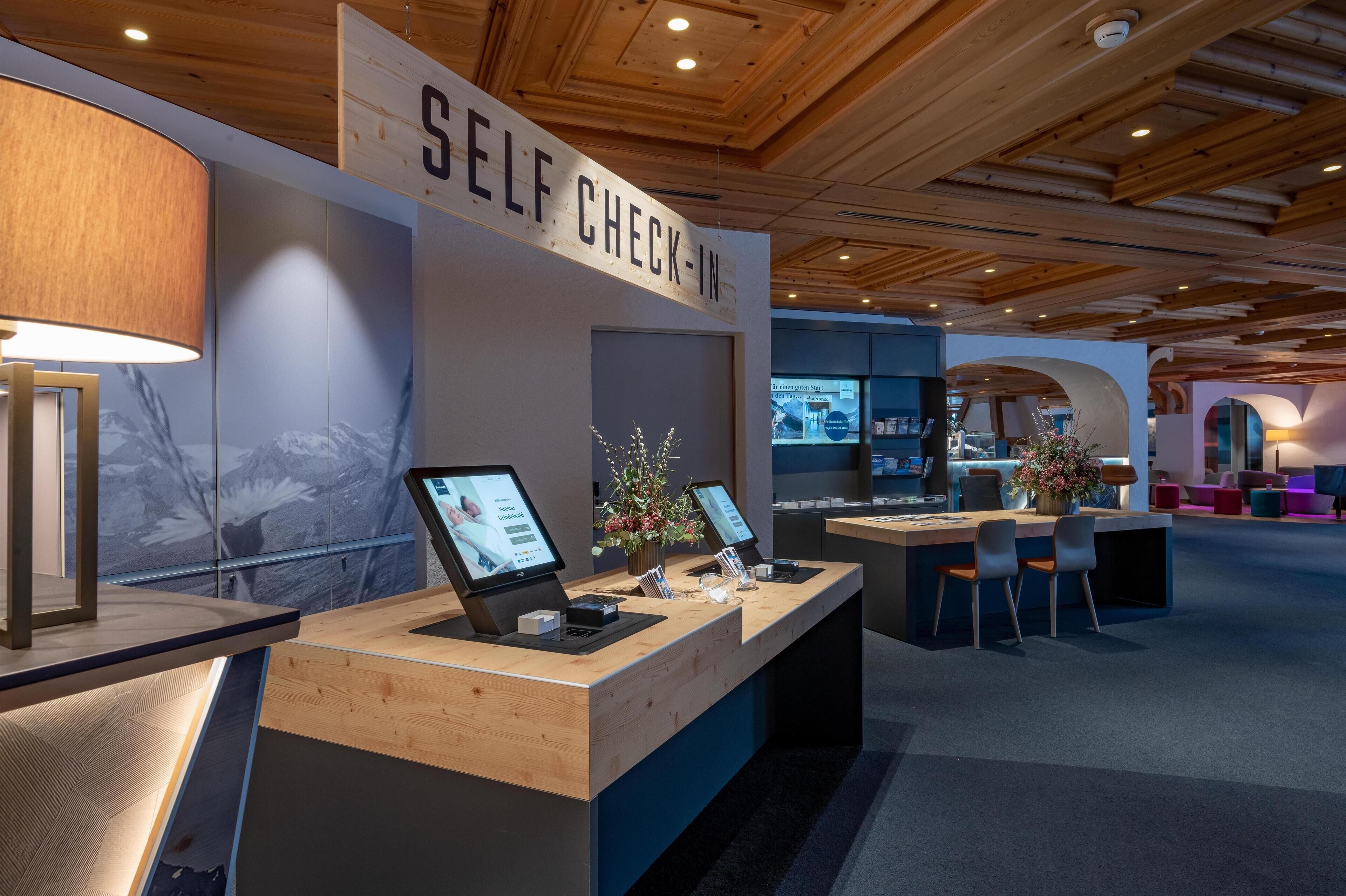A self-check-in area with wooden counters, digital kiosks, and a sign indicating self-service.