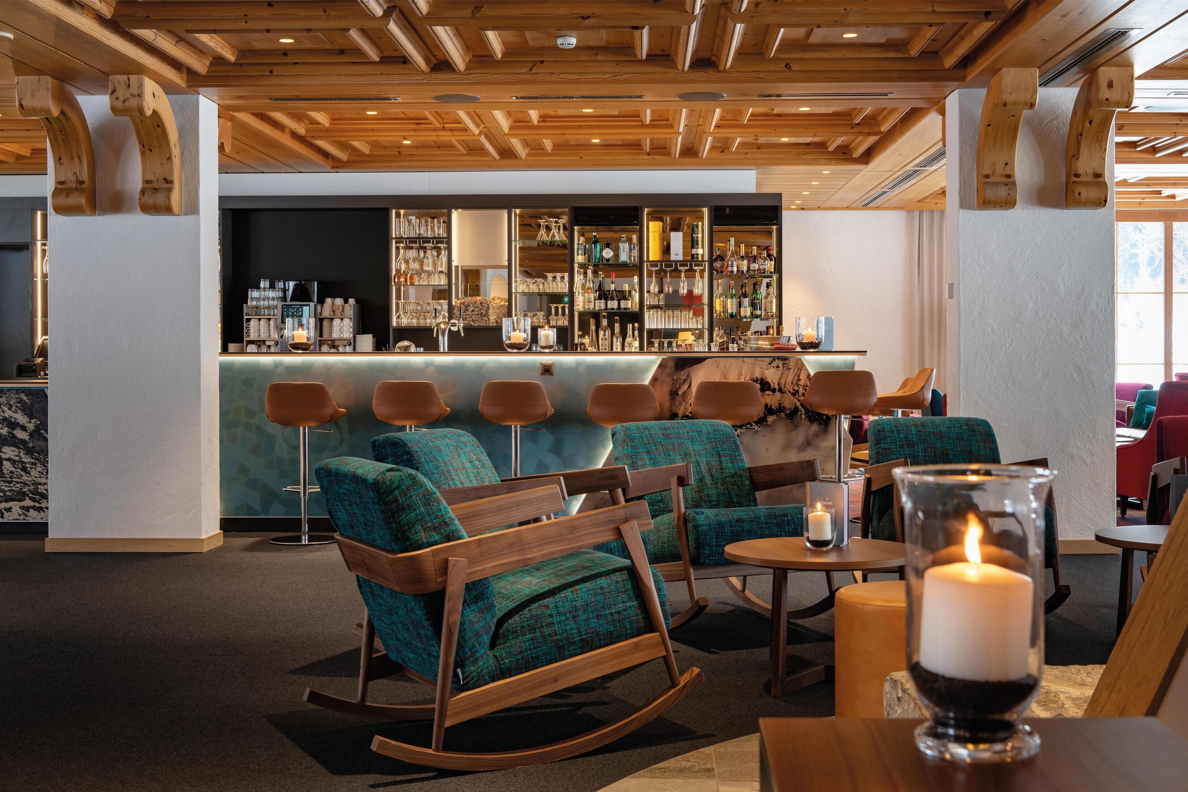 A bar area with wooden ceiling beams, teal upholstered chairs, and a bar stocked with bottles.