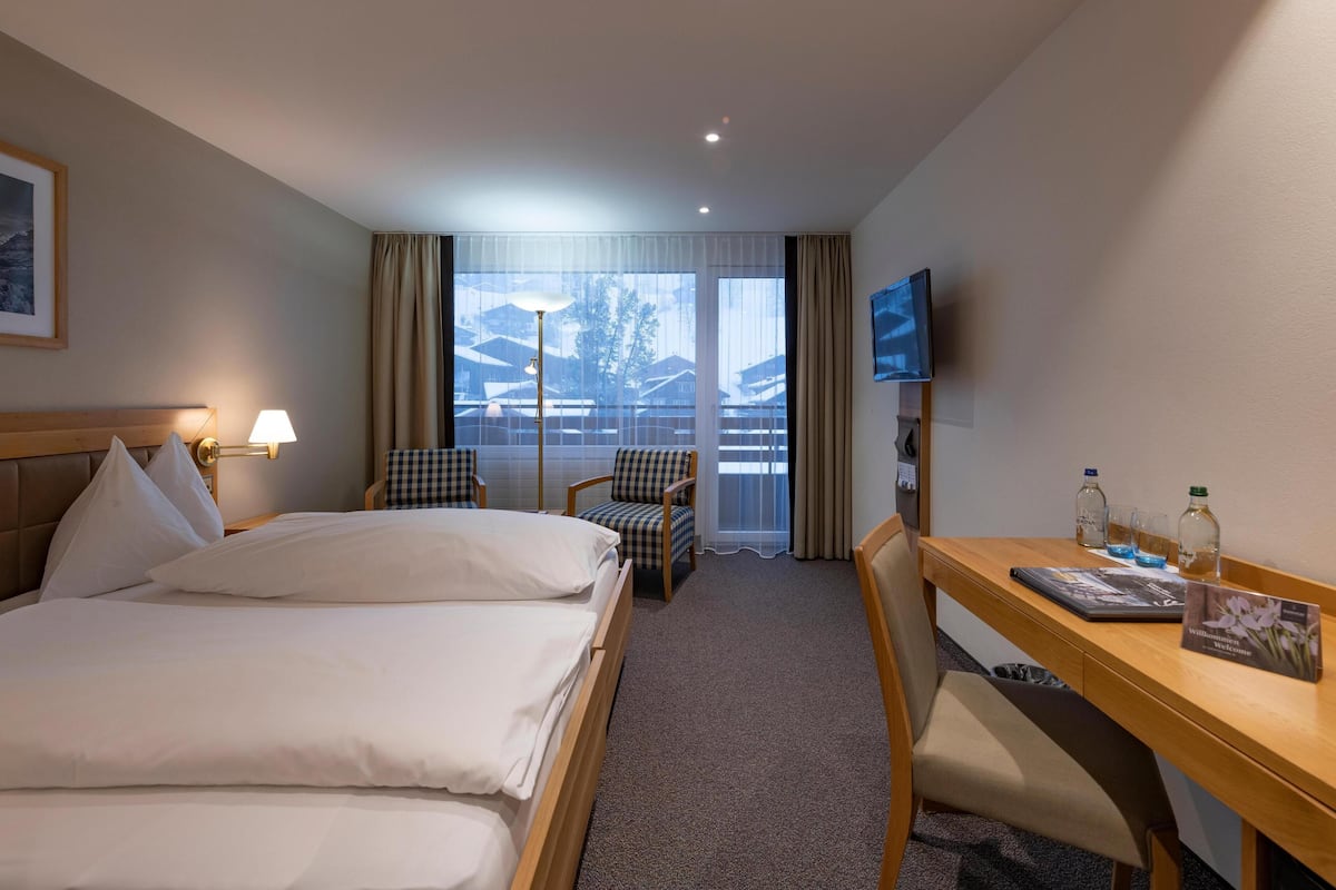 Une chambre d’hôtel équipée d’un lit, d’un bureau, d’une chaise, d’une télévision et d’une fenêtre avec des rideaux.