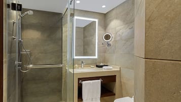 Un baño moderno con ducha envuelta en cristal, tocador con espejo y retrete.