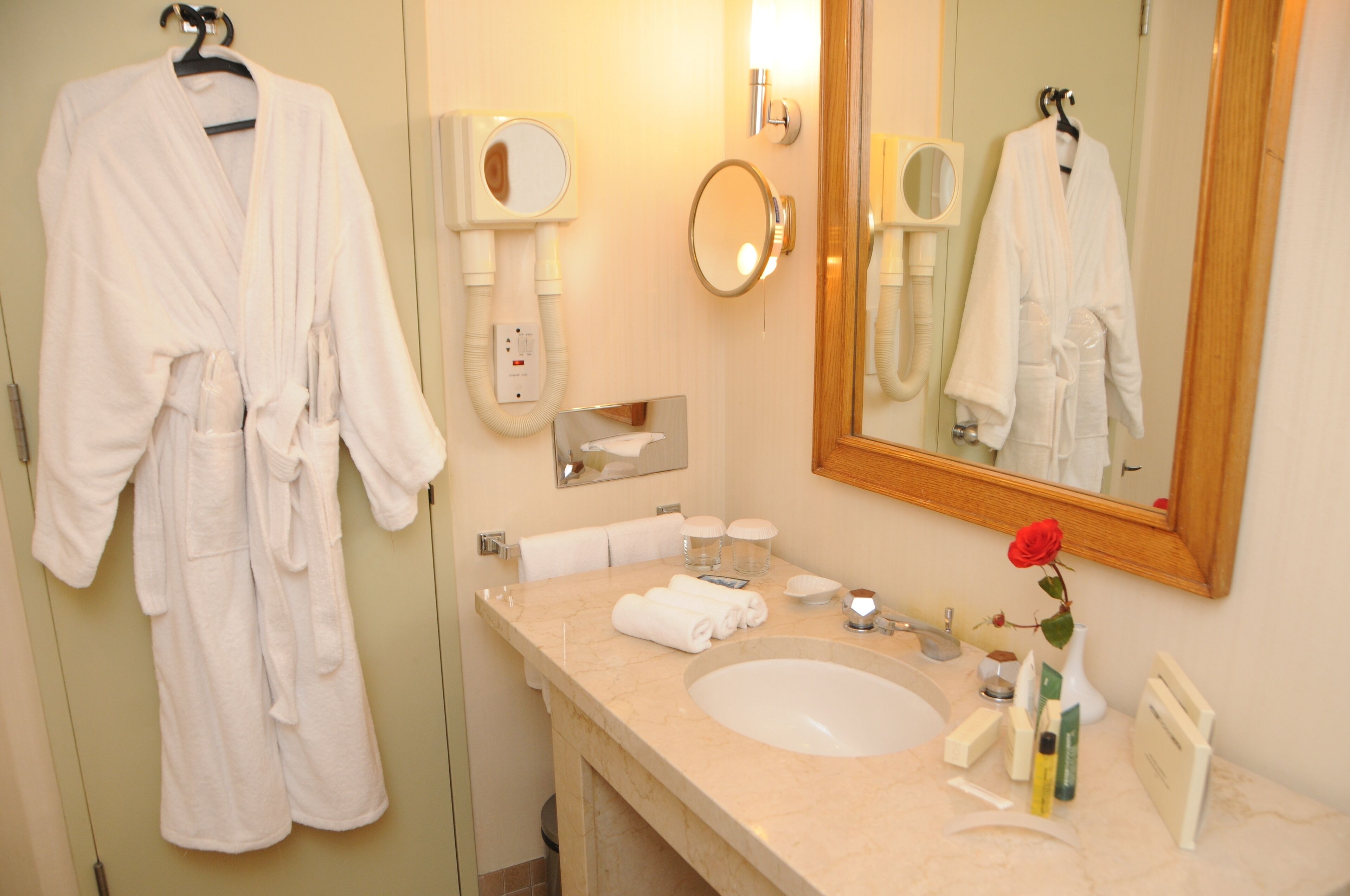 A bathroom with a large mirror, a sink, and two white robes hanging on hooks.