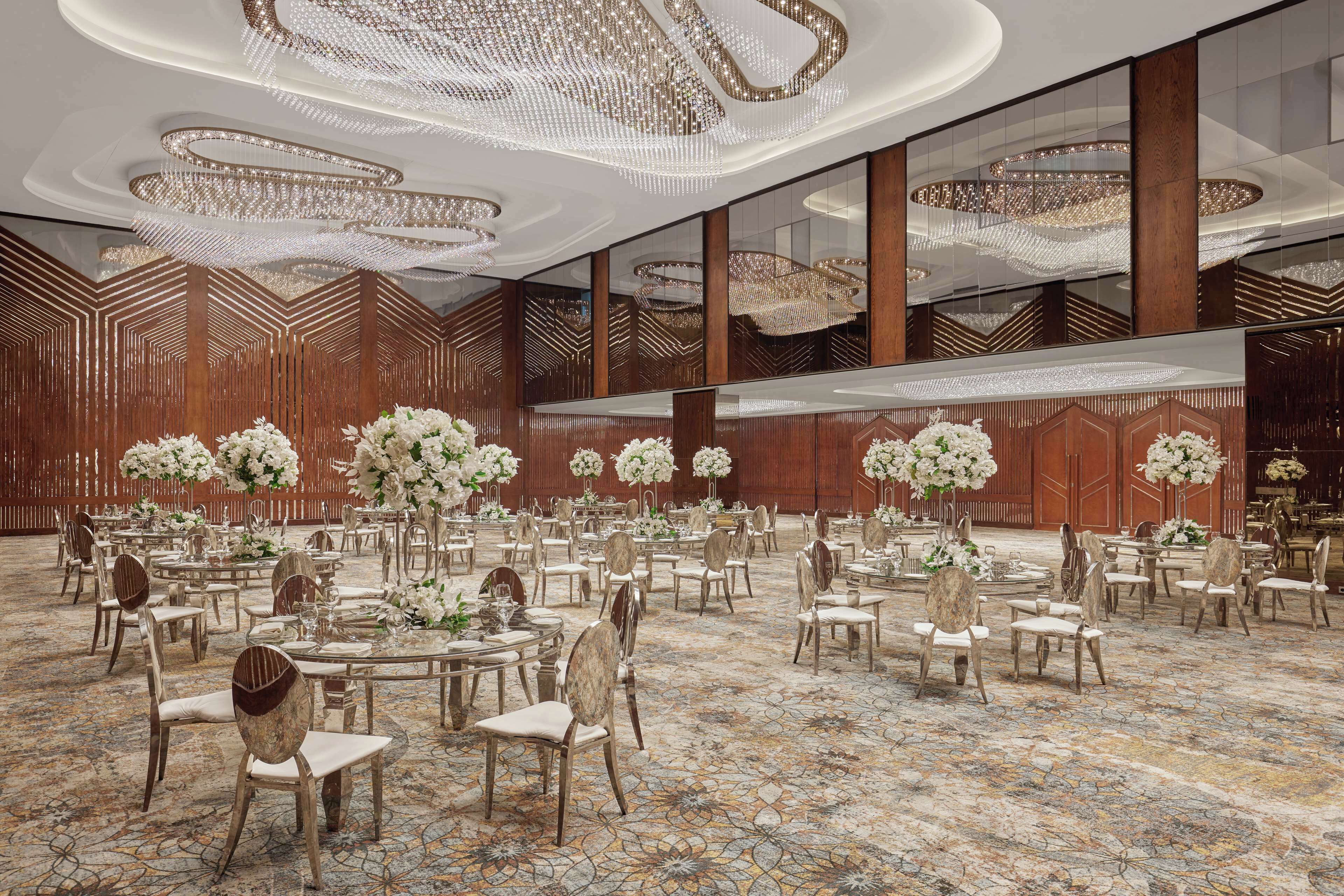A spacious banquet hall with round tables, elegant chairs, and large floral centerpieces.