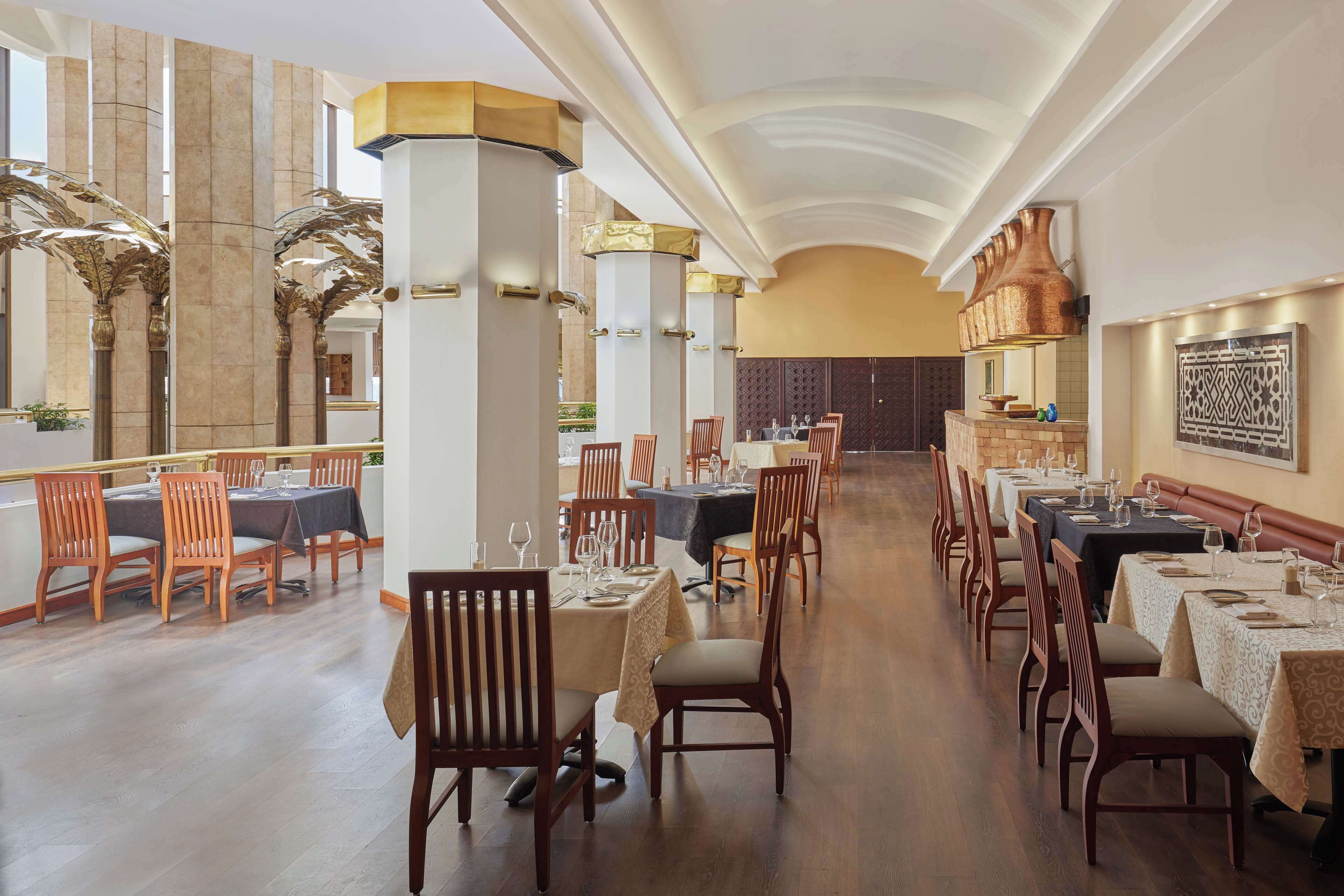 Un vaste espace dédié à la salle à manger, avec de nombreuses tables et chaises, de hauts plafonds et des colonnes décoratives.