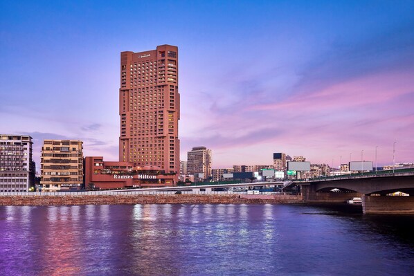A high-rise hotel with multiple floors, a prominent sign, and a view of the city skyline across a body of water.