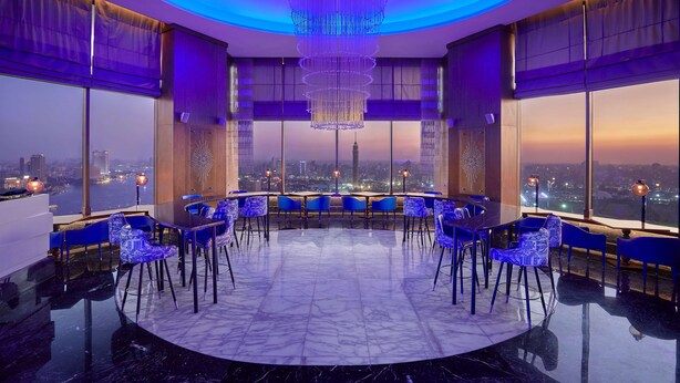 A modern bar with a circular layout, large windows, and a city view.