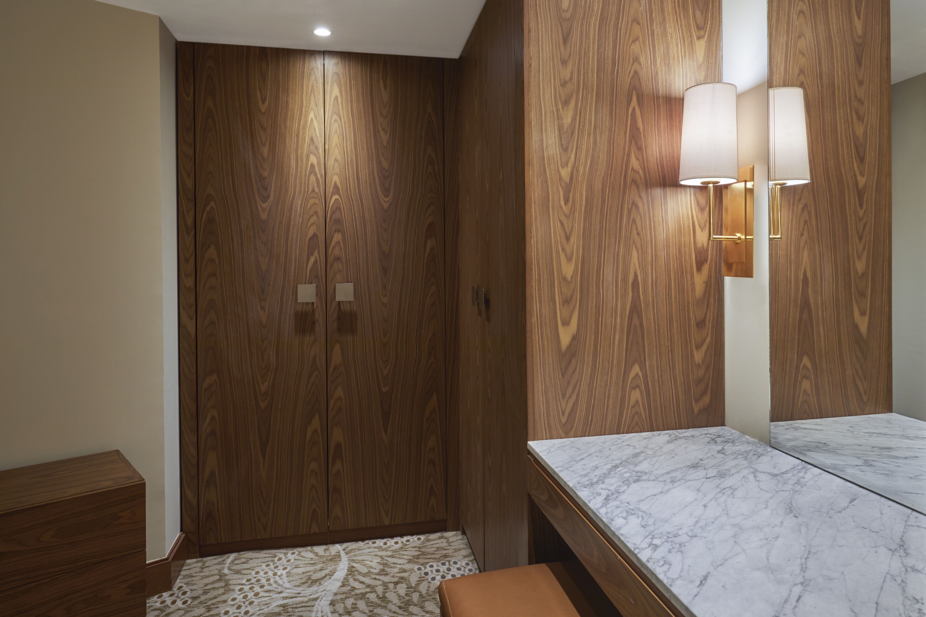 Un baño moderno con muebles de madera, encimera de mármol e iluminación empotrada.