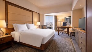 A hotel room with a large bed, a desk, a television, and a city view.
