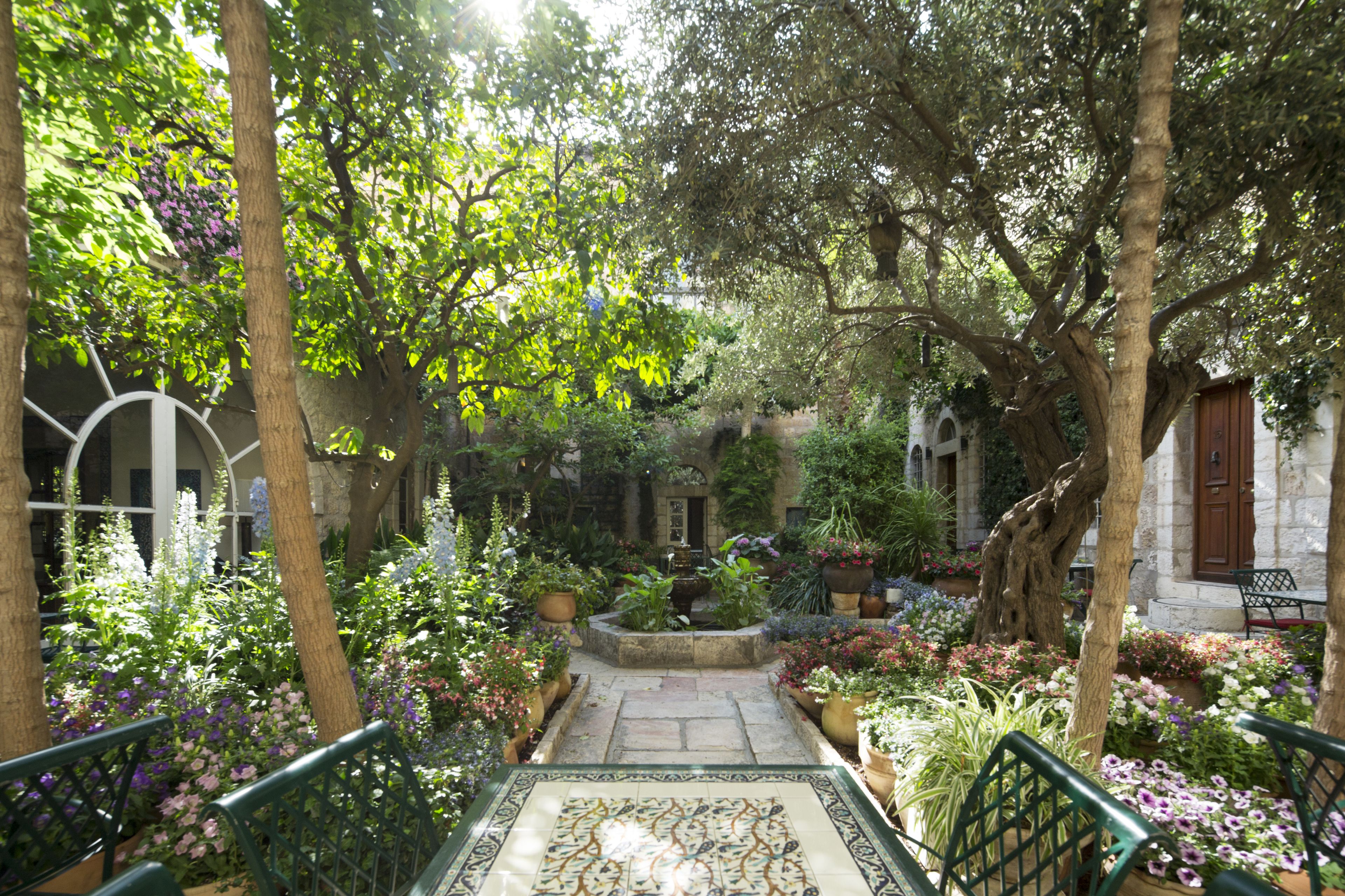 Une cour avec une fontaine, entourée de plantes en pot et de bancs.