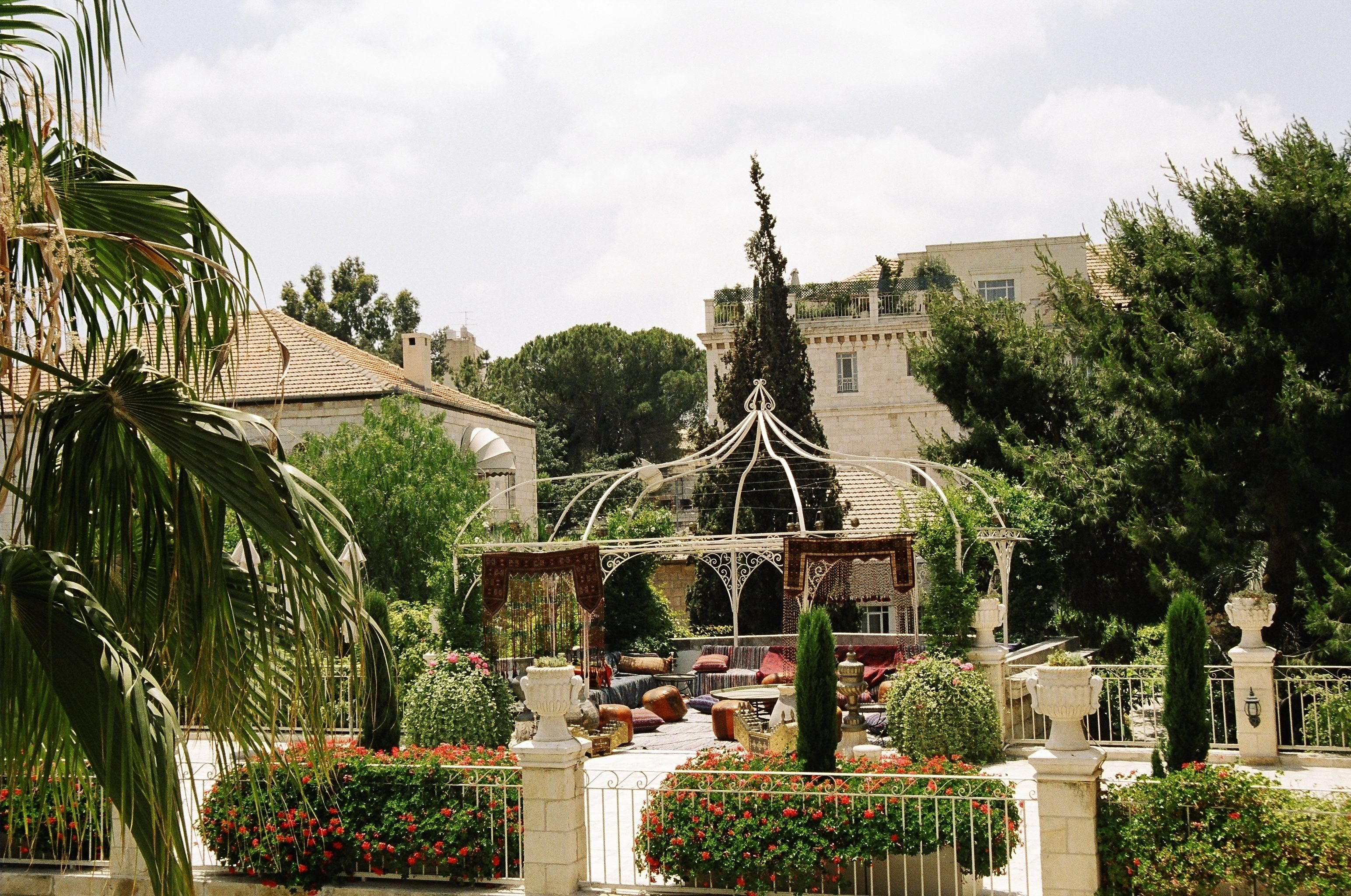 An outdoor seating area with tables and chairs, surrounded by lush greenery and flowering plants.