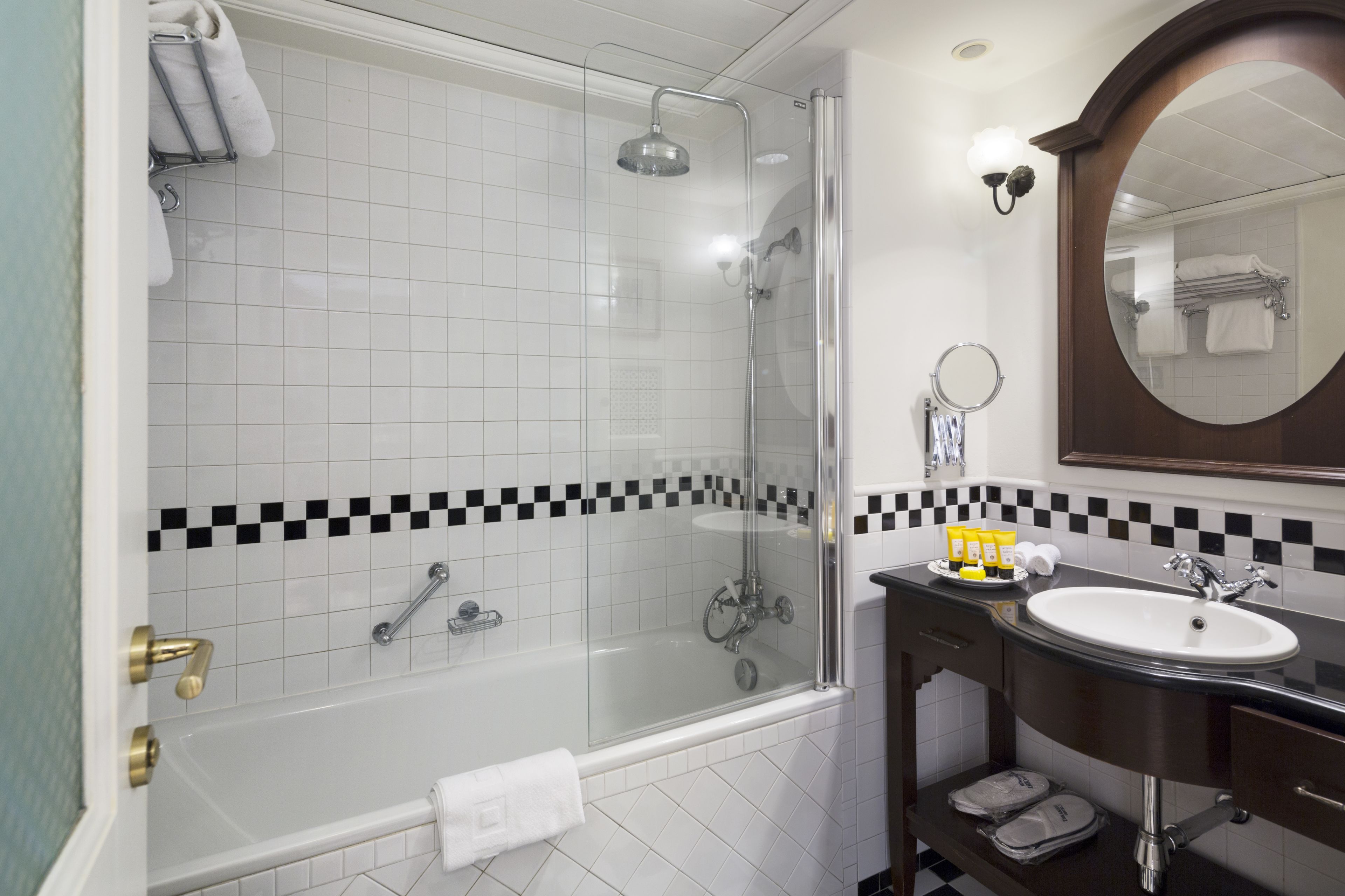 A modern bathroom with a glass-enclosed shower, a white bathtub, a sink with a mirror, and a checkered tile backsplash.