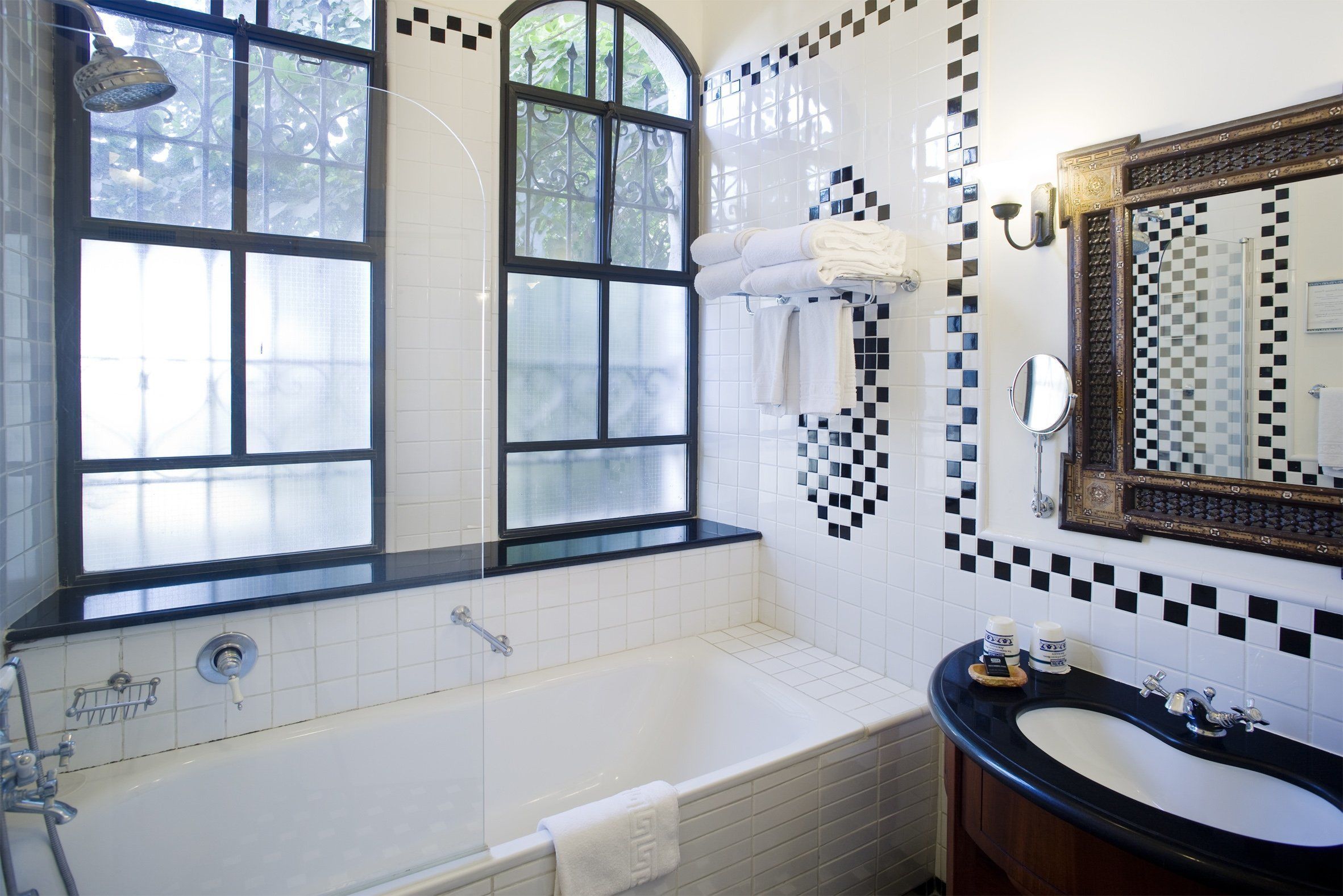 A bathroom with a bathtub, a sink, and a large mirror. There are towels hanging on the wall and a window with a view of trees.