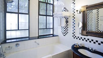 A bathroom with a bathtub, a sink, and a large mirror. There are towels hanging on the wall and a window with a view of trees.