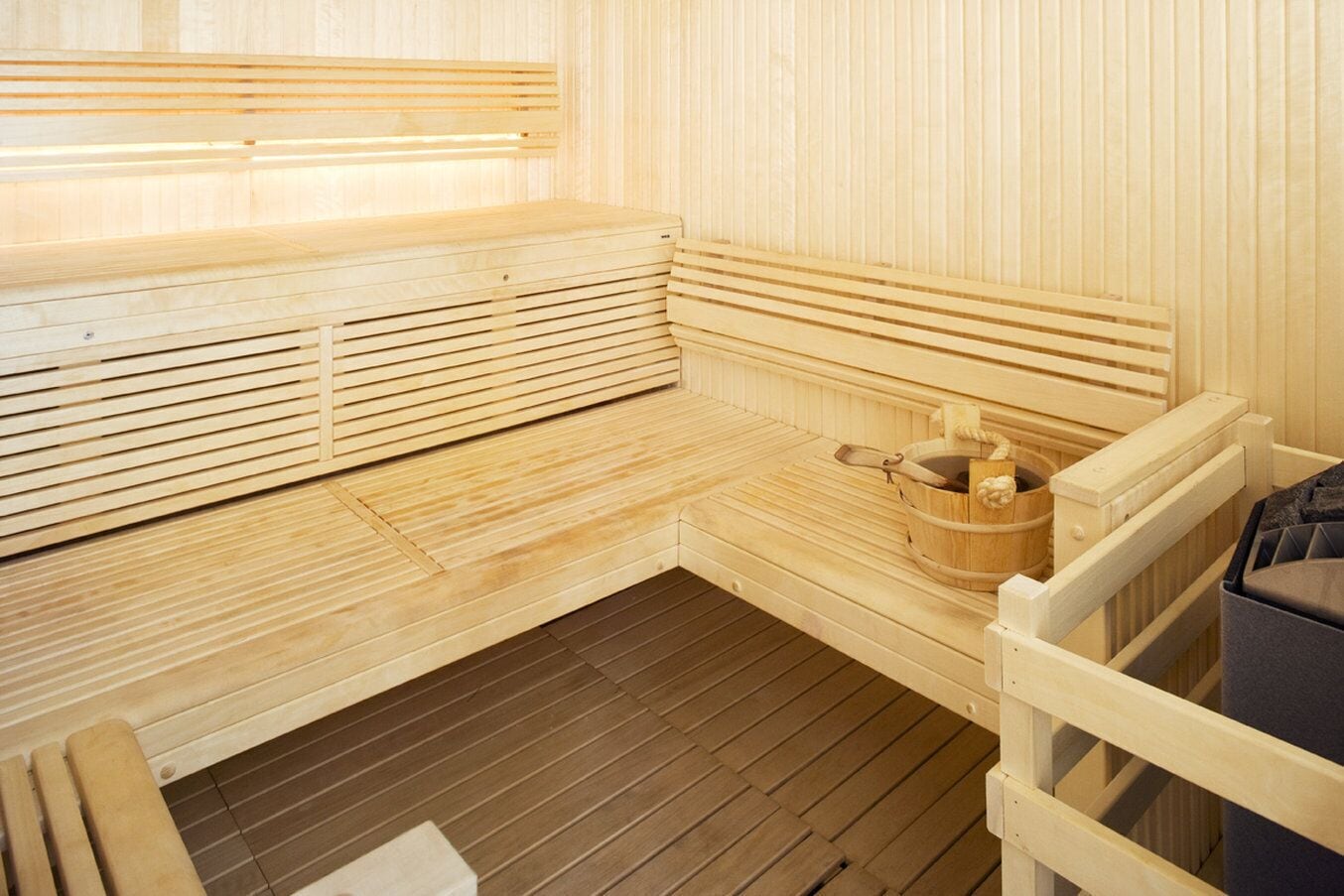 A wooden sauna with benches and a bucket of stones.