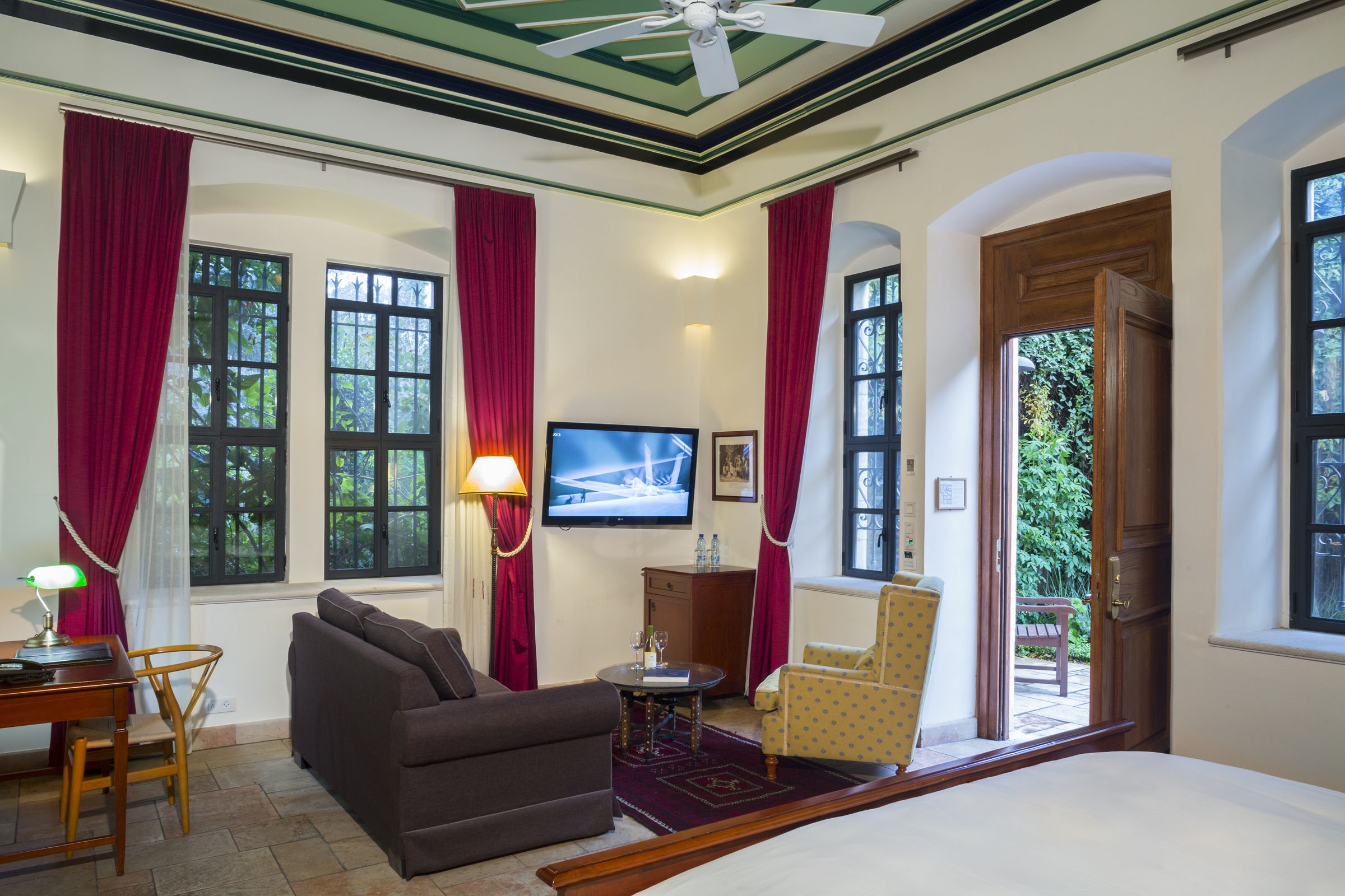 A hotel room with a bed, a sofa, a desk with a lamp, a TV, and a view of the outdoors.
