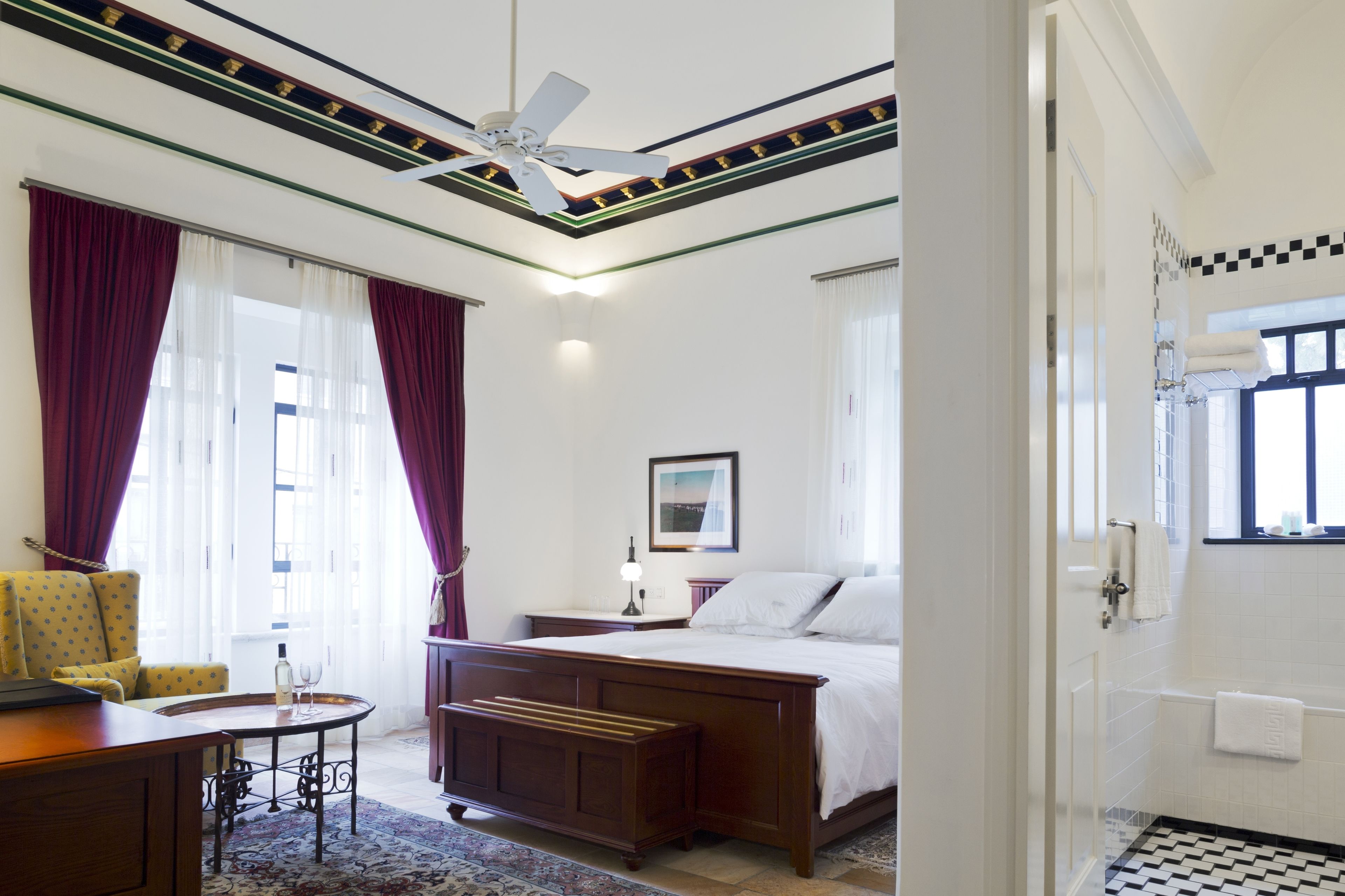 Quarto de hotel com cama, escrivaninha, cadeira e janela com cortinas.