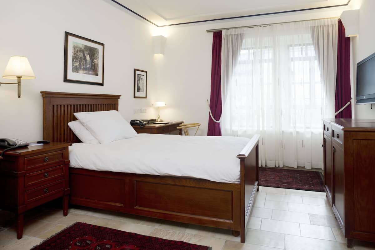 A neatly arranged bedroom with a wooden bed, bedside tables, a desk, and a television.