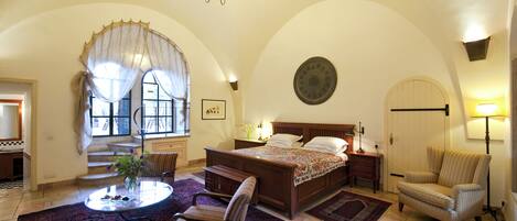 Una camera da letto con un letto grande, un angolo salotto con tavolo e sedie, un lampadario e vista all'esterno da una finestra.