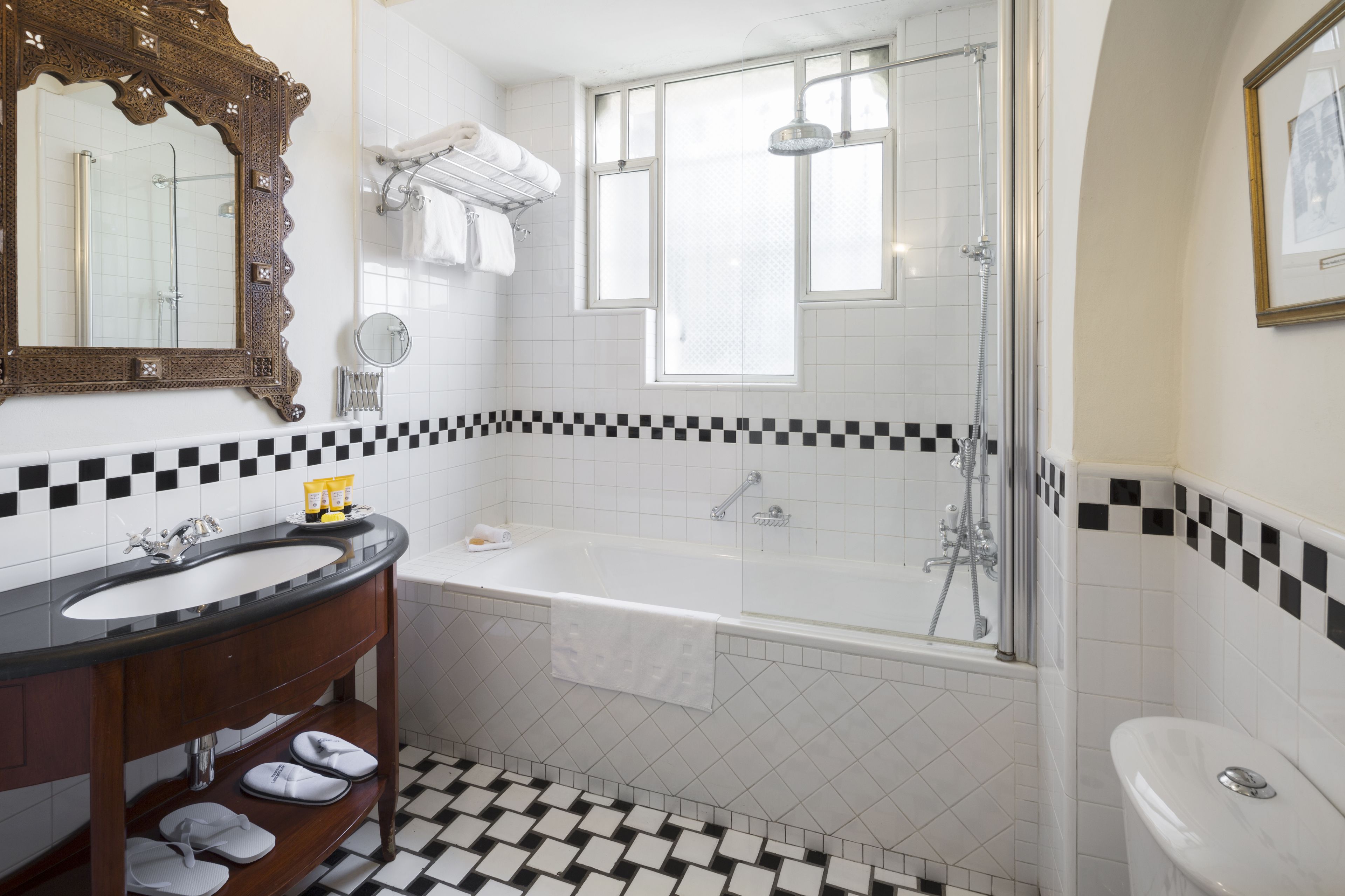 Um banheiro com piso xadrez preto e branco, uma banheira branca, uma pia branca e um espelho grande com moldura decorada.