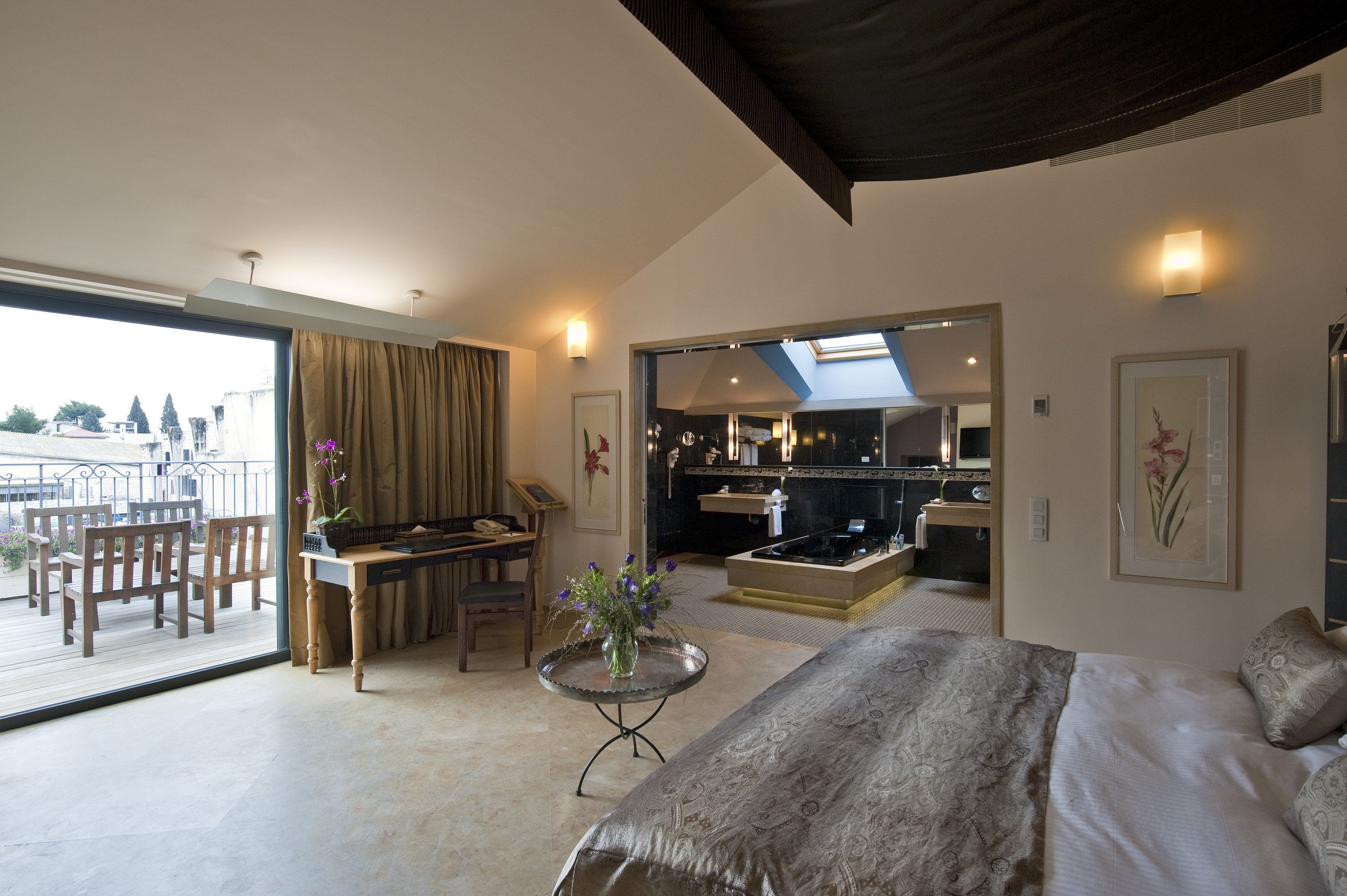 A modern bedroom with a large bed, a dining area with a table and chairs, a kitchen area, and a balcony with a view.