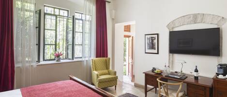 Un dormitorio con una cama grande, un escritorio, una silla, un televisor y una ventana con cortinas.