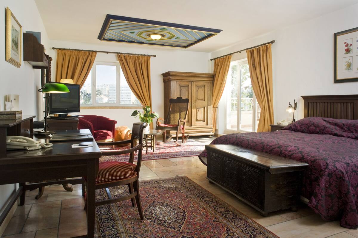 A hotel room with a bed, desk, chair, and a large window.