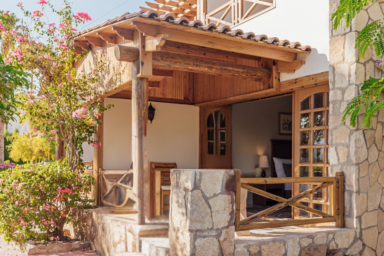 Un edificio rústico de madera con fachada de piedra, una pérgola de madera y una escalera de piedra que lleva a una puerta de madera.