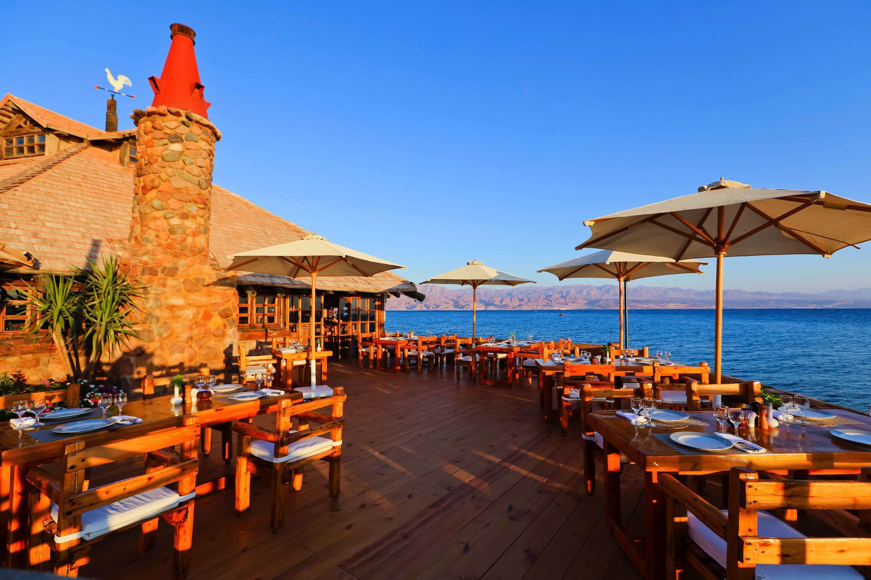 A wooden deck with tables and chairs, overlooking a body of water.