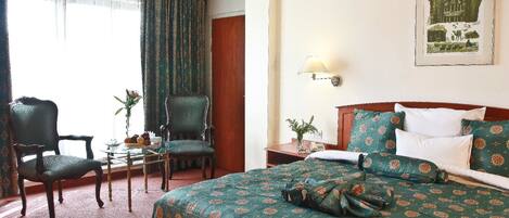 Een hotelkamer met een groot bed, een stoel, een klein tafeltje en een lamp.