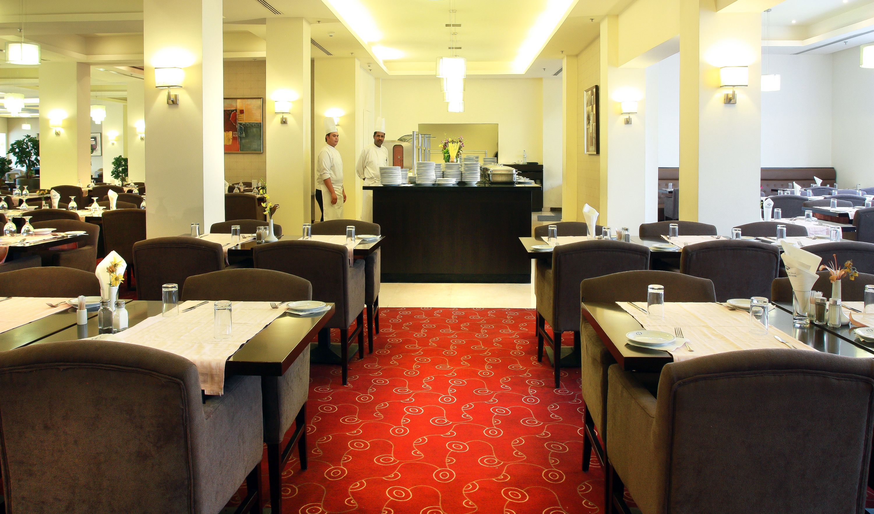 A hotel dining area with multiple tables, chairs, and a central counter.