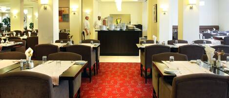 A hotel dining area with multiple tables, chairs, and a central counter.