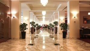 A hotel corridor with marble floors, potted plants, chandeliers, and wall sconces. - Grand Palace Hotel (Amman)