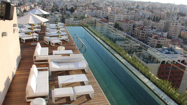 A rooftop pool area with lounge chairs and a glass barrier overlooking a cityscape. - Grand Palace Hotel (Amman)