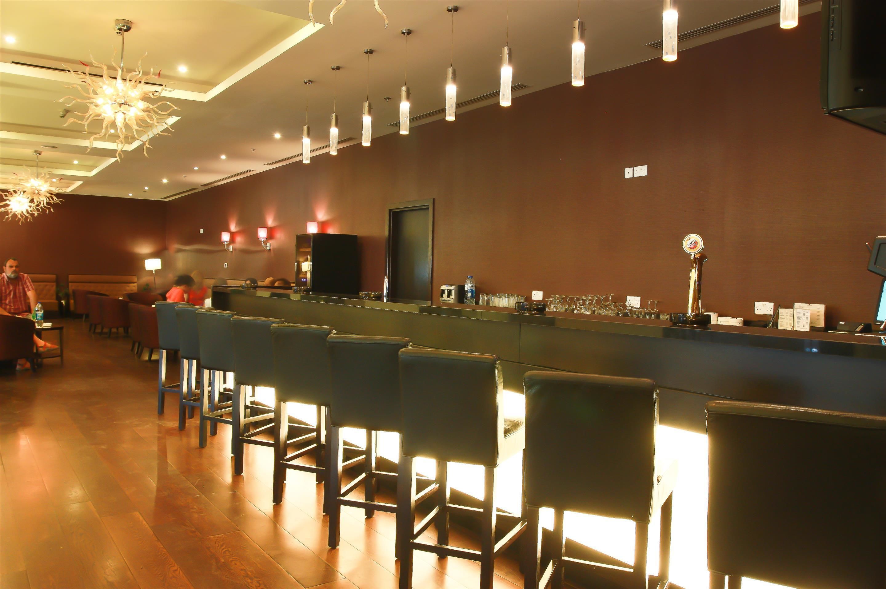 Un espace bar doté d’un long comptoir, de nombreux tabourets et de luminaires suspendus.