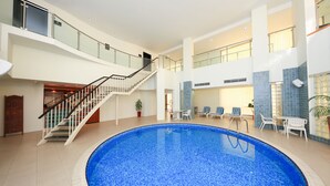 A large indoor swimming pool with a glass balustrade, a staircase, and lounge chairs.