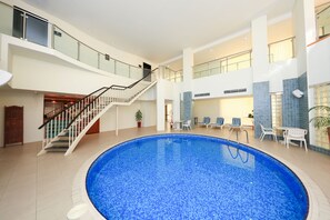 A large indoor swimming pool with a glass balustrade, a staircase, and lounge chairs.