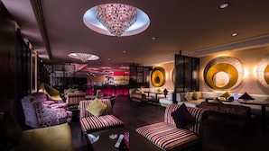 A modern lounge area with striped sofas, a bar in the background, and decorative wall lighting.